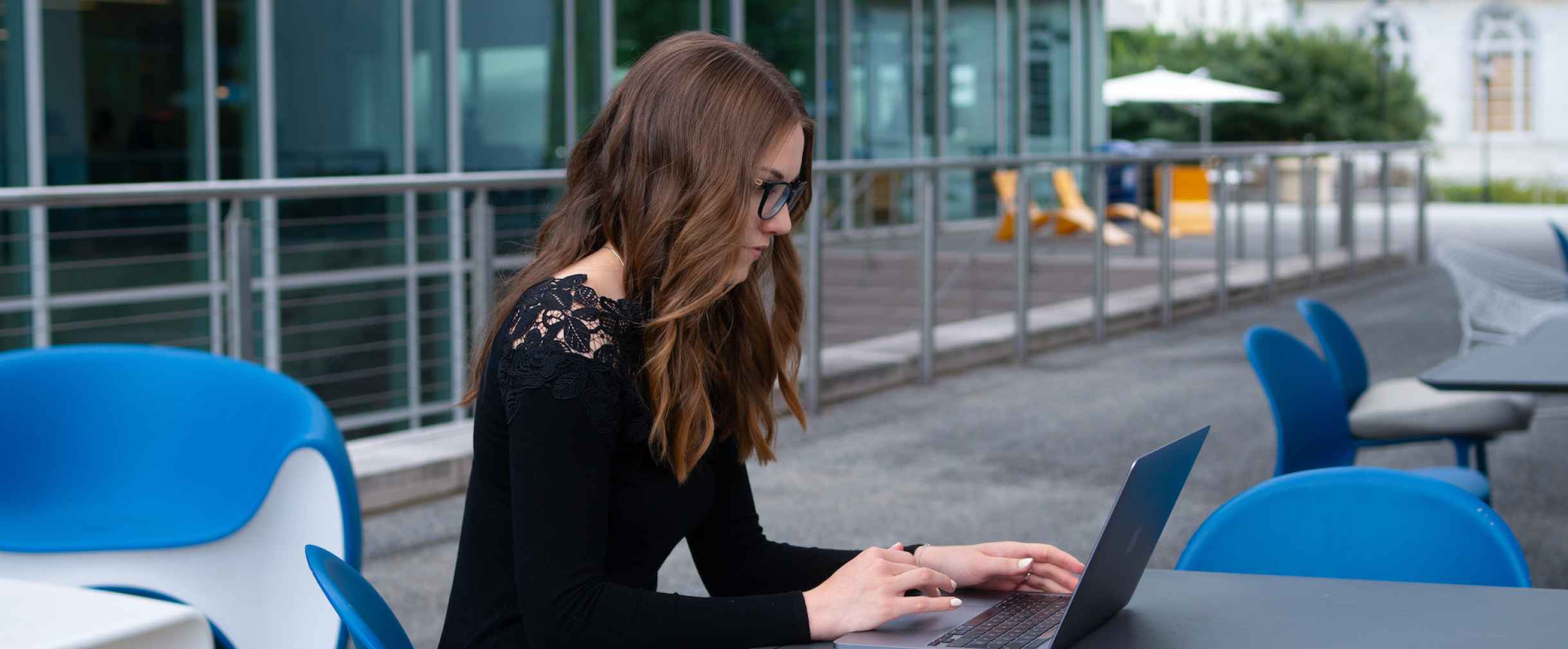 Student sitting at an outdoor table looking at laptop.