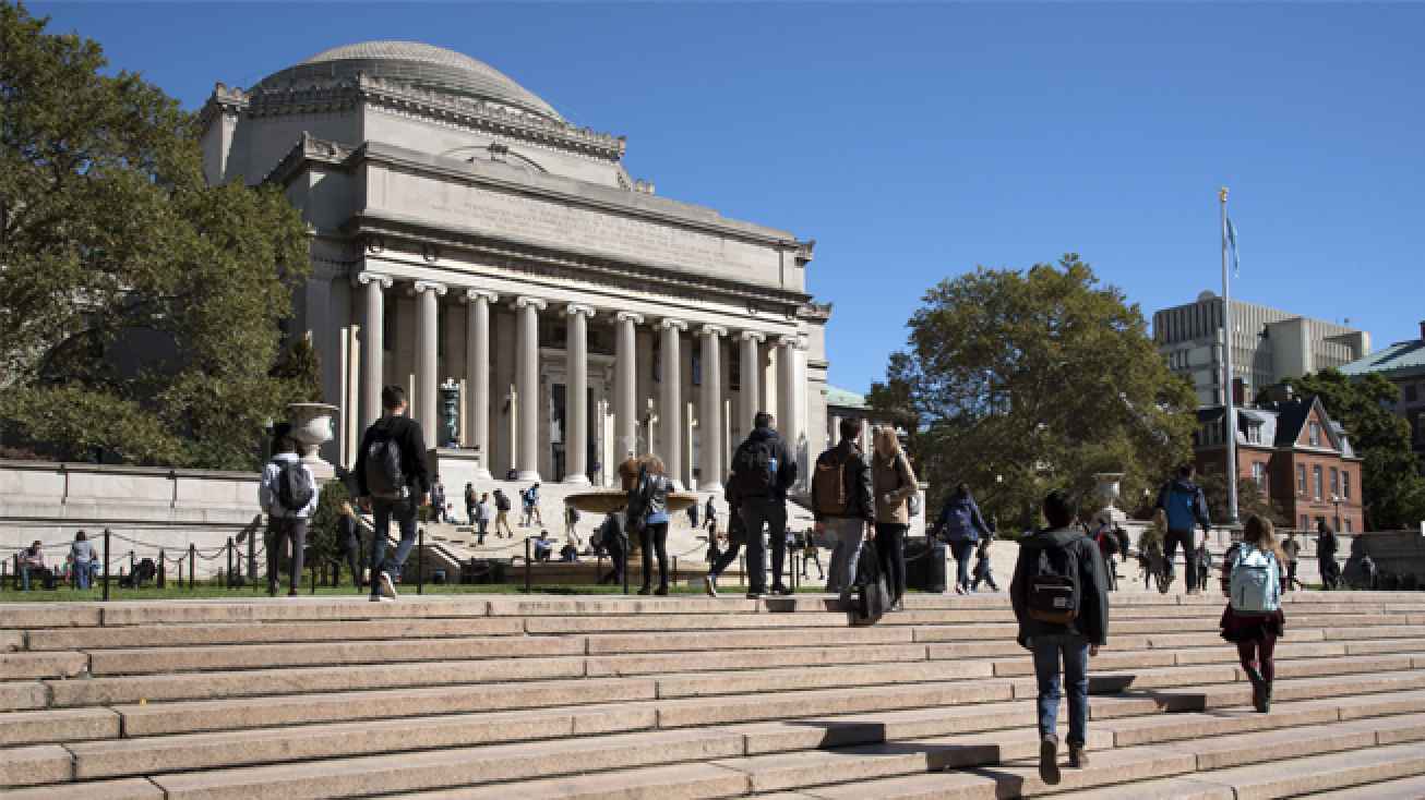 Students walking up stairs in front of a university building on a sunny day